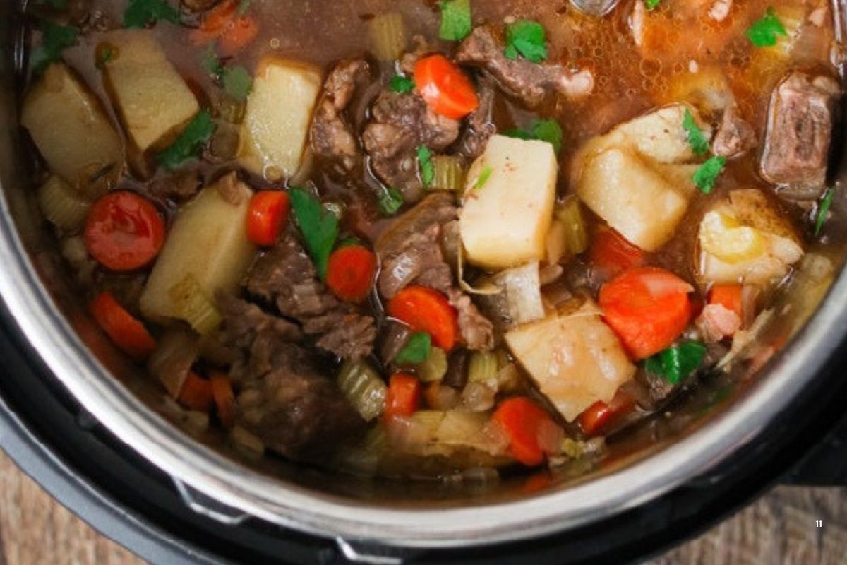 Overhead view of hearty pork stew in an Instant Pot, filled with tender pork, potatoes, carrots, celery, and fresh herbs in a rich broth.