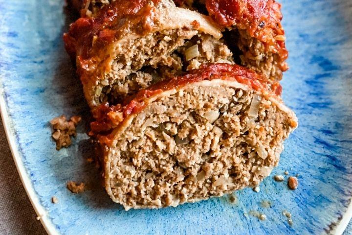 Bacon Wrapped Meatloaf sits sliced on a turquoise blue plate.