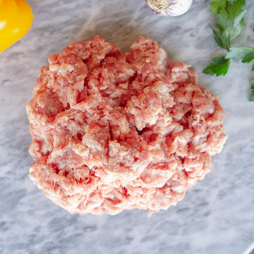 A closeup picture of raw Pederson's Whole30 Approved ground pork is shown loose on a marble cutting board.