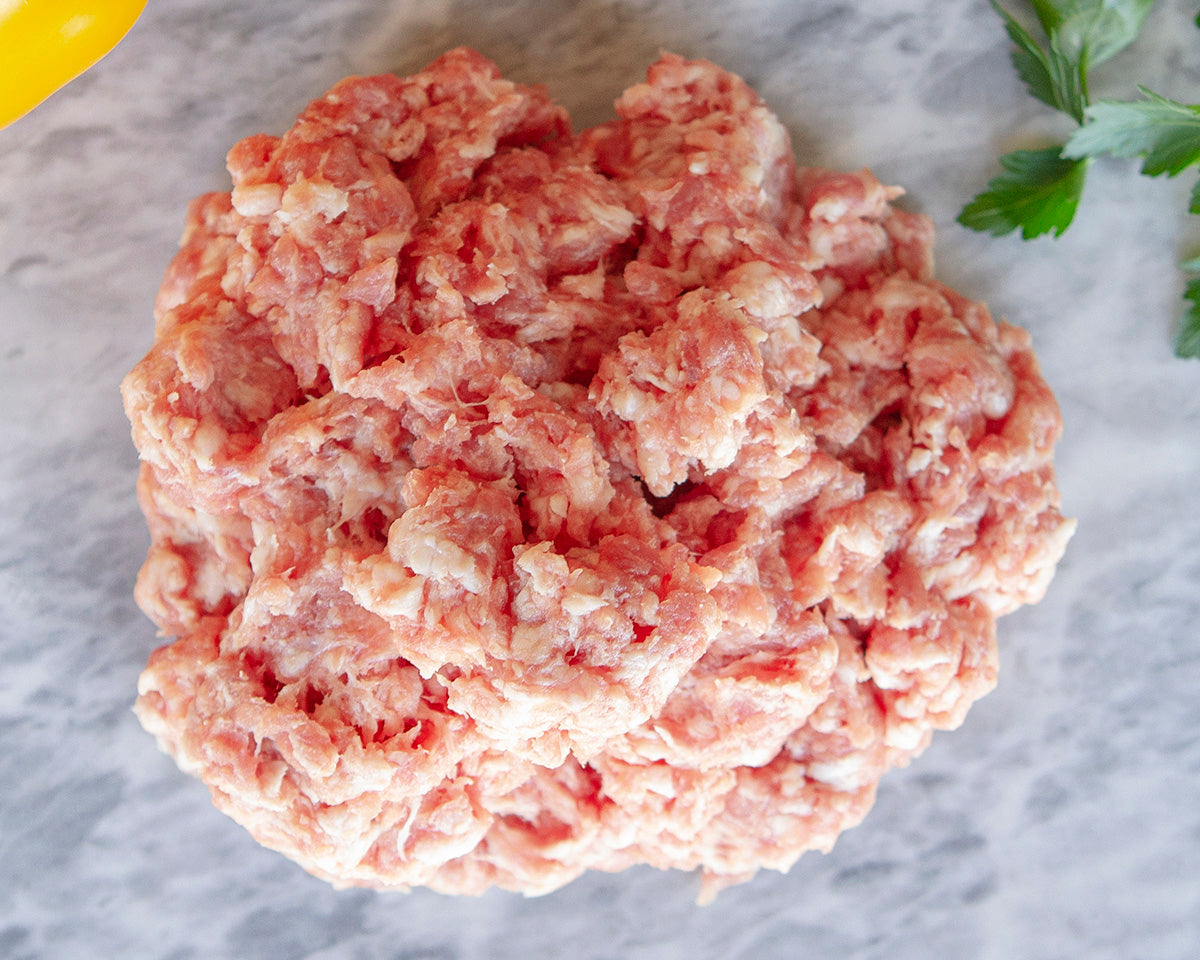 A closeup picture of raw Pederson's Whole30 Approved ground pork is shown loose on a marble cutting board.